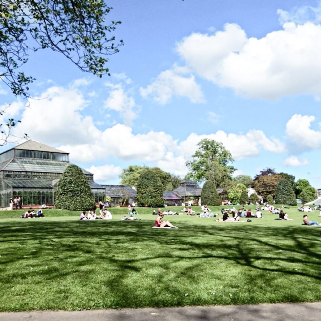 Image of a group of people sitting infront of a large beautiful glass building in a park